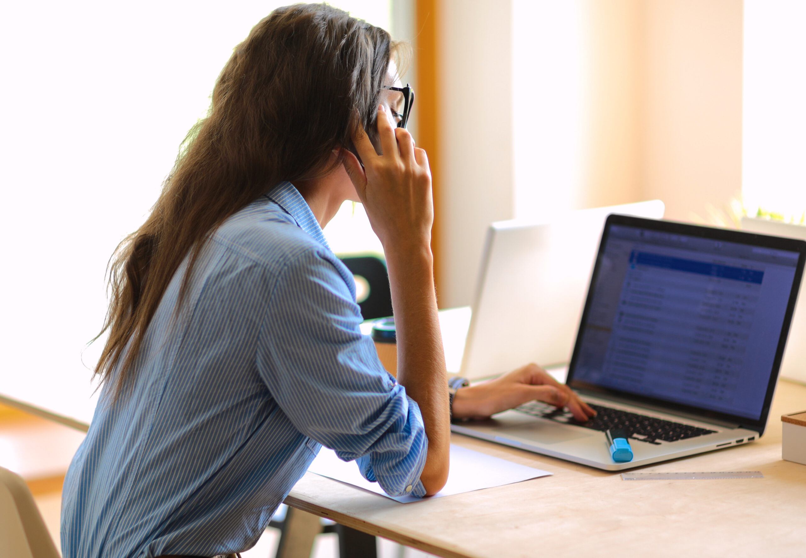 Beautiful young business woman sitting at office desk and talking on cell phone