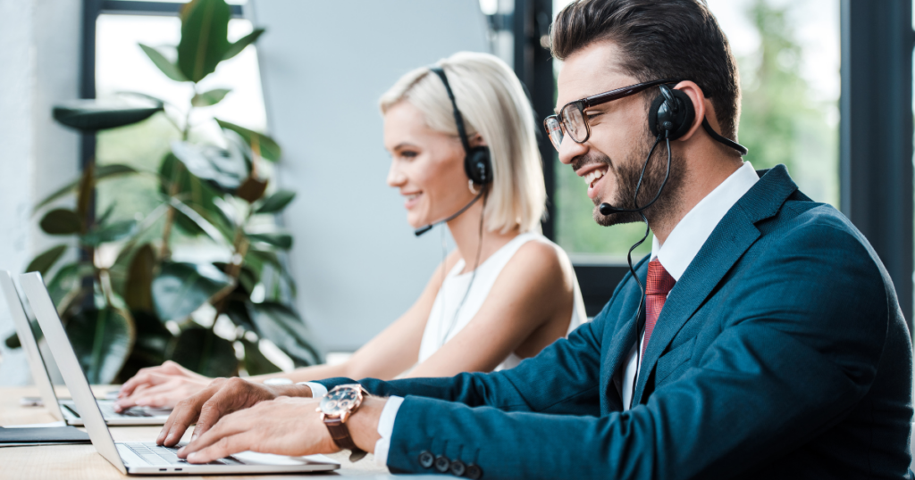 Call Centers versus Omni-Channel Contact Centers. What is the difference? Happy man wearing a headset and working on laptop with female coworker doing the same in background