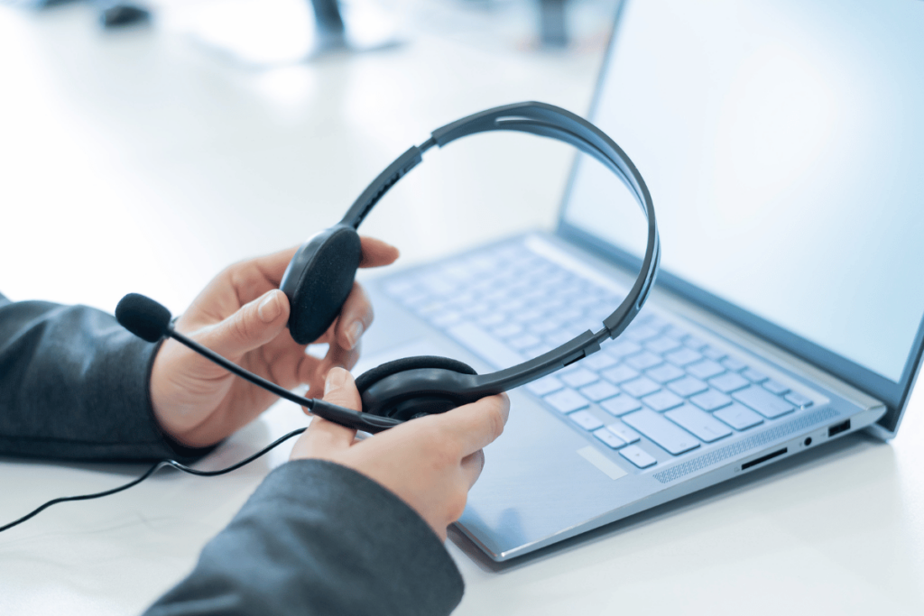 Will AI Replace Contact Centers? Close-up of female hands with a headset over a laptop. Unrecognizable woman working in a support service took off her headphones.