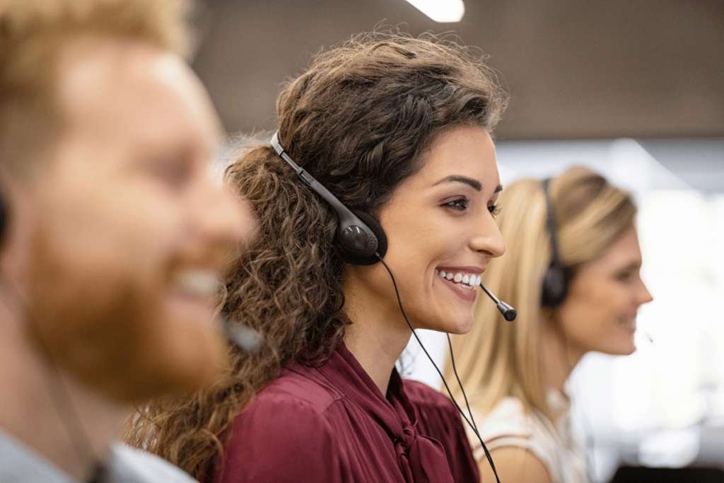 three call center employees are smiling from the side view, and the focus is on the female in the middle while the other two are blurred.