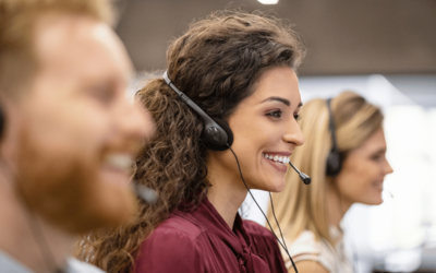 three call center employees are smiling from the side view, and the focus is on the female in the middle while the other two are blurred.