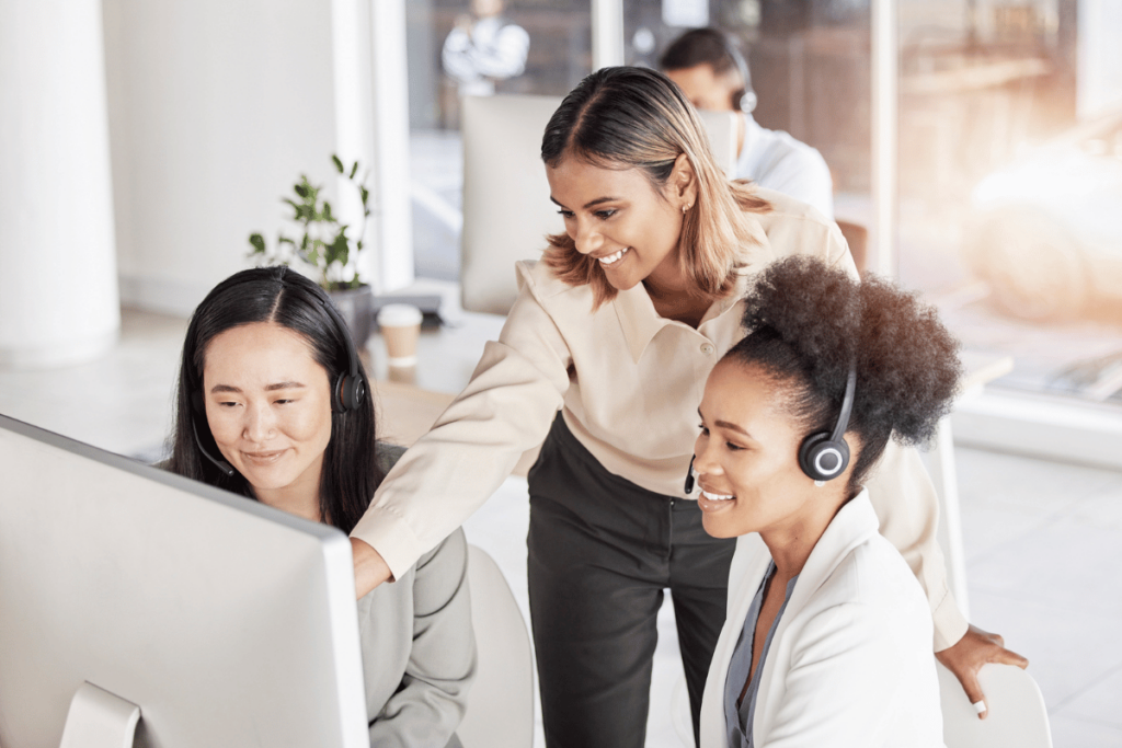 Can Call Coaching Actually Improve Your Bottom Line? A group of women at a call center smile and look at the computer screen. One woman is training the others.