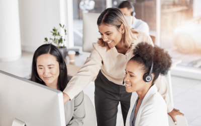 Can Call Coaching Actually Improve Your Bottom Line? A group of women at a call center smile and look at the computer screen. One woman is training the others.