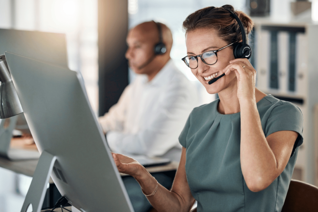 a professional woman wearing a headset smiles while looking at her large screen computer