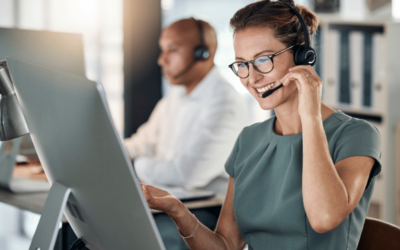 a professional woman wearing a headset smiles while looking at her large screen computer