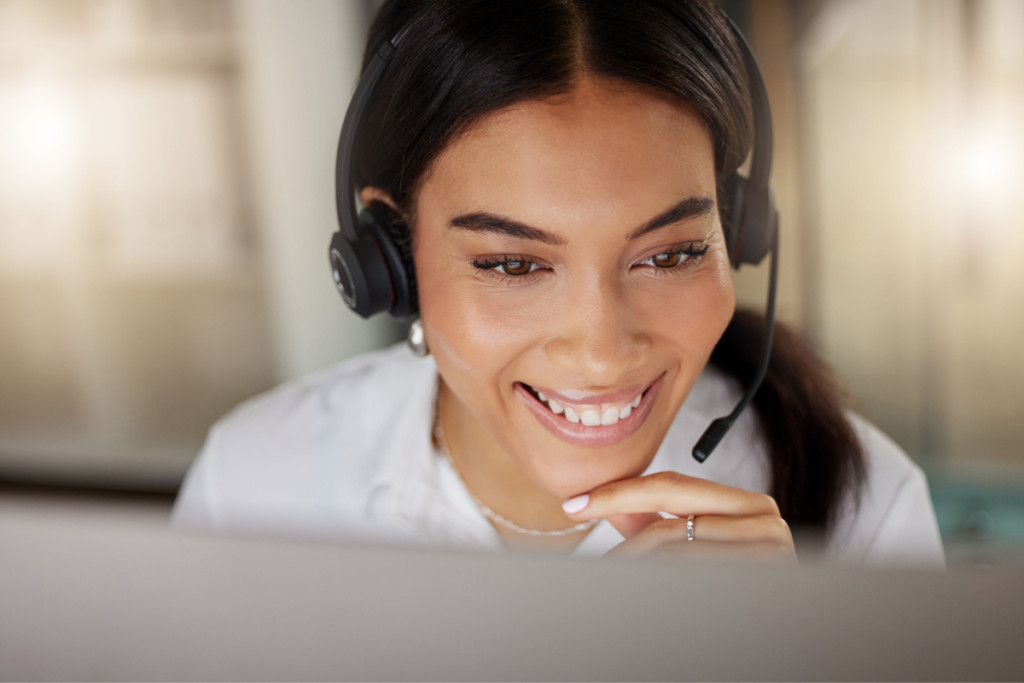 How to Get Started with AI Quality Assurance - A smiling call agent wears a headset and looks toward her computer.