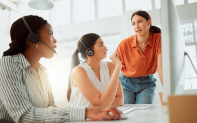 How to Get Started with Quality Assurance Coaching and Training Programs. Two women at a call center wear headphones and listen to a third woman coaching them.